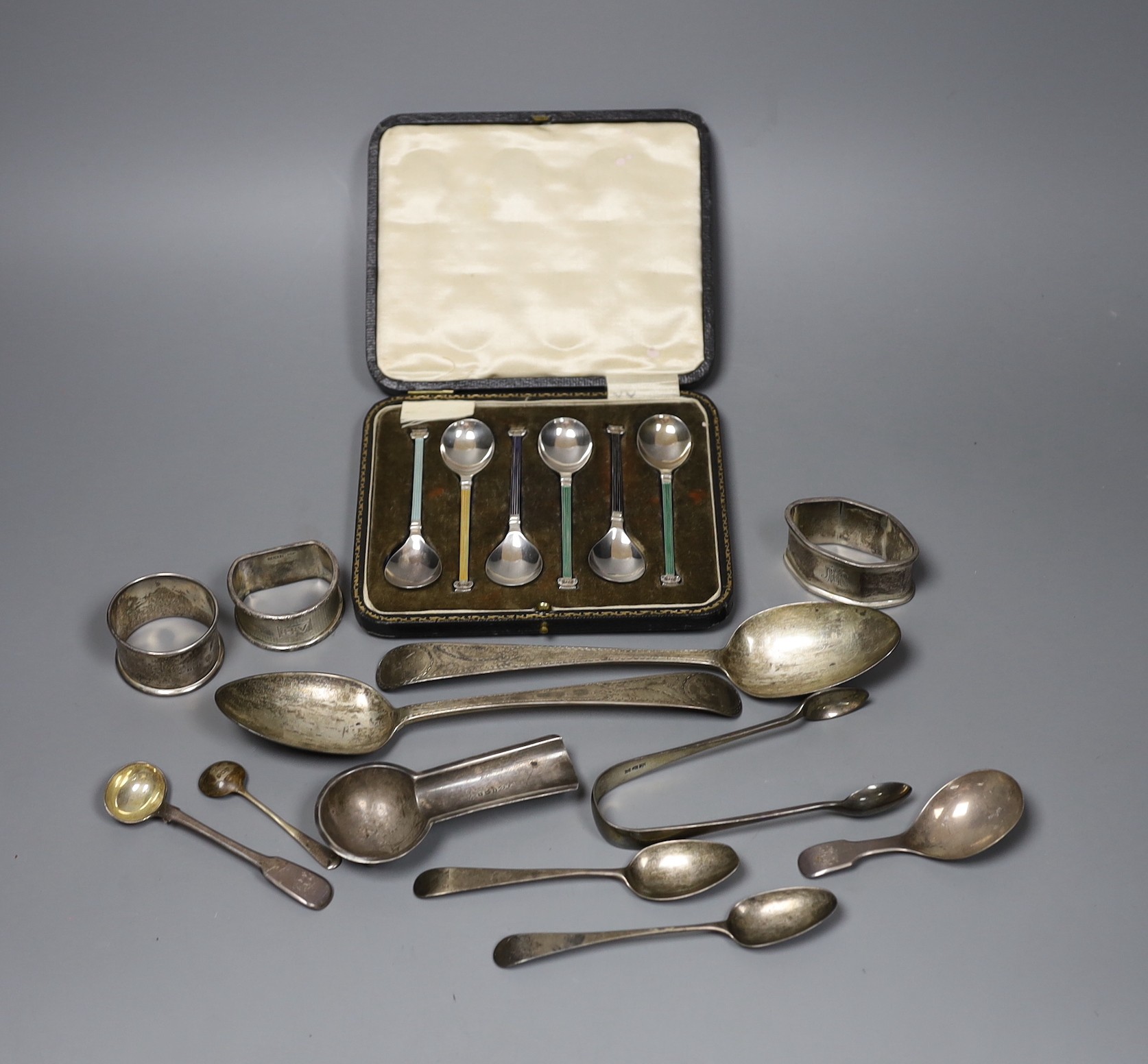 A pair of George III bright cut silver table spoons, three later assorted napkin rings, a cigar stand, a pair of tongs, five assorted spoons, 10oz., and a cased set of silver and enamel coffee spoons